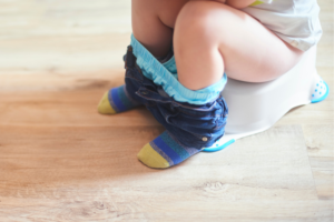 Child sitting up potty. We only see legs and feet. bottoms are down by ankles. demonstrates the correct sitting position when going potty
